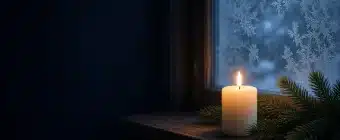 A single candle glowing beside evergreen branches on a dark winter night